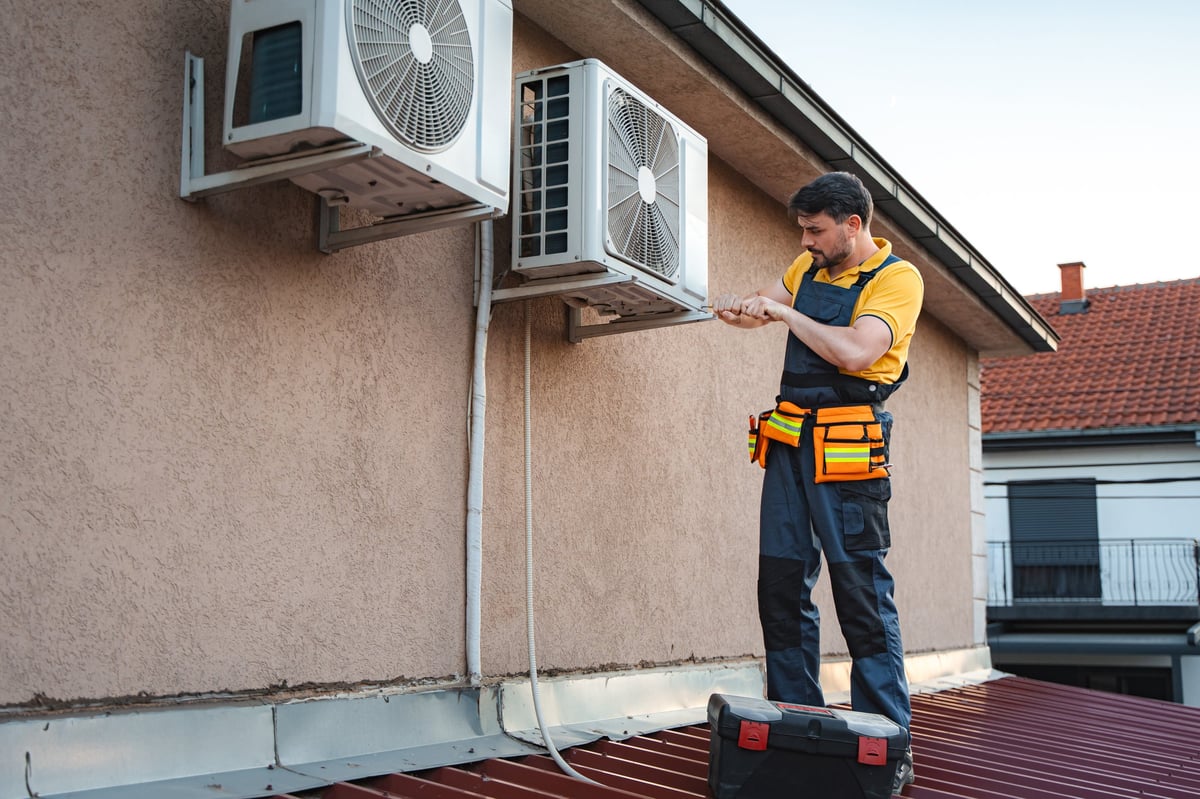 Technician installing an exterior air conditioning unit on a house wall